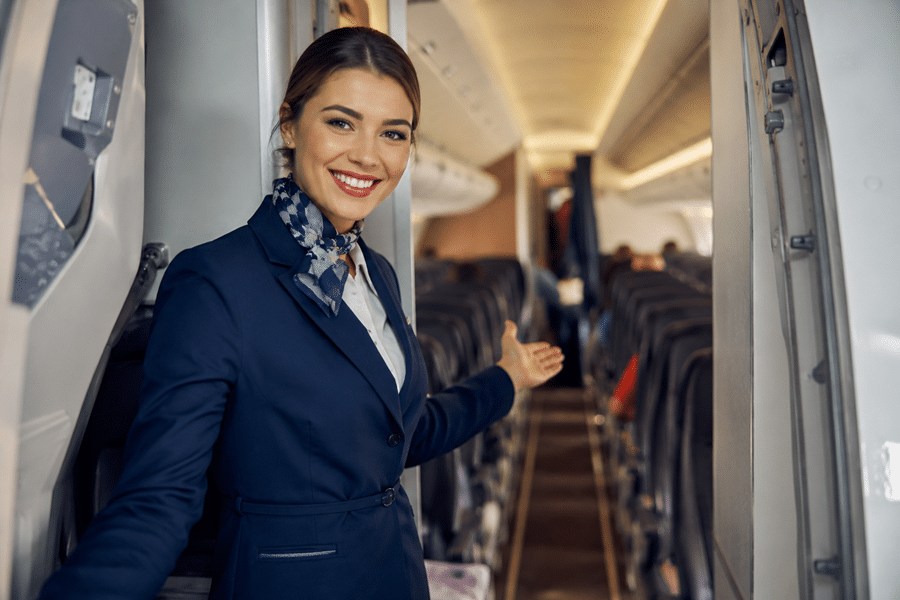 Flight attendant in a navy uniform greeting passengers at the aircraft door with a welcoming smile and open cabin.